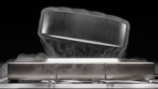 A black hockey puck is shown levitating above a metallic rectangular platform, surrounded by visible vapor or mist.