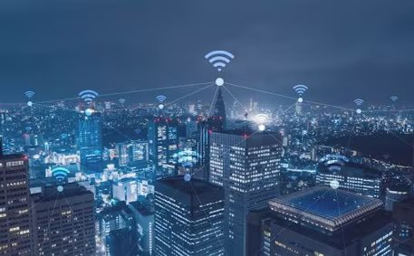 A nighttime cityscape features illuminated skyscrapers and buildings, overlaid with digital icons representing wireless network connections.