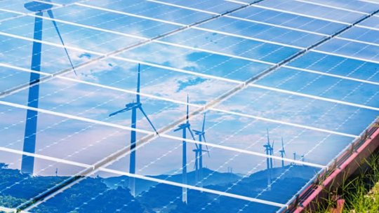 A close-up view of solar panels reflecting the sky and several wind turbines.