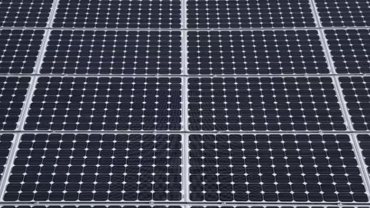 A detailed, close-up view of multiple solar panels arranged in a grid pattern. The panels feature a repeating array of photovoltaic cells with visible metallic grid lines.