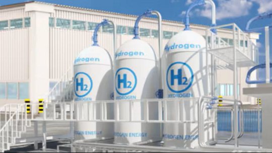Industrial hydrogen storage tanks labeled ‘H₂’ and ‘Hydrogen’ connected to pipes and equipment outside a large industrial building under a blue sky.
