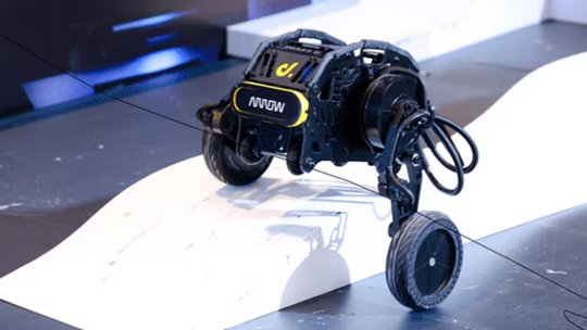 Ein kompaktes, vierrädriges Robotik-Gerät steht auf einer weißen, geneigten Rampe in einer Innenumgebung.