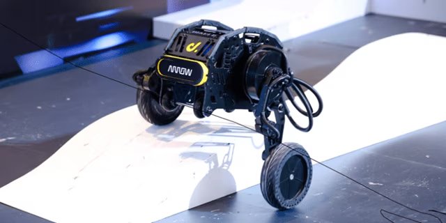 Ein kompaktes, vierrädriges Robotikgerät befindet sich auf einer weißen, geneigten Rampe in einer Innenumgebung.