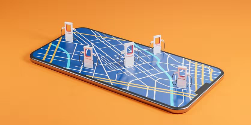 A large smartphone lies flat with a digital map displayed on its screen. Several miniature gas station pumps are positioned on the map, representing fuel station locations.