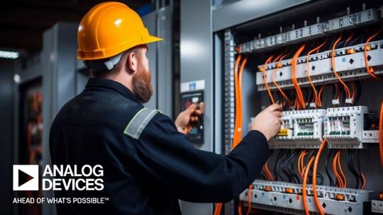 노란색 안전모를 착용한 남성 엔지니어가 주황색 케이블과 회로 차단기로 가득 찬 열린 전기 제어 패널을 조사하고 있습니다. 장면은 밝게 비춰지며 배선과 장비의 복잡성이 강조됩니다. Analog Devices 로고와 문구 'AHEAD OF WHAT'S POSSIBLE™'가 왼쪽 하단에 뚜렷하게 표시됩니다.