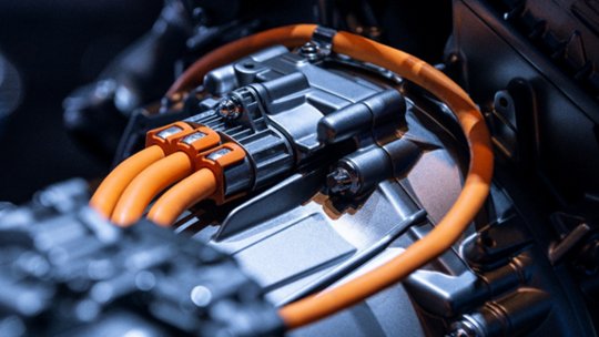 A detailed view of an electric vehicle motor highlights prominent orange high-voltage cables connected to the metallic engine housing. 