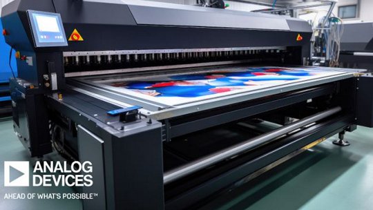 A high-capacity large format printer is actively printing a vibrant, colorful image in an industrial workspace. The machine is surrounded by clean, modern equipment and the floor is a polished green. The text 'ANALOG DEVICES' and 'AHEAD OF WHAT'S POSSIBLE' is clearly visible in the lower left corner.