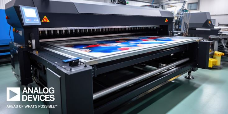 A high-capacity large format printer is actively printing a vibrant, colorful image in an industrial workspace. The machine is surrounded by clean, modern equipment and the floor is a polished green. The text 'ANALOG DEVICES' and 'AHEAD OF WHAT'S POSSIBLE' is clearly visible in the lower left corner.
