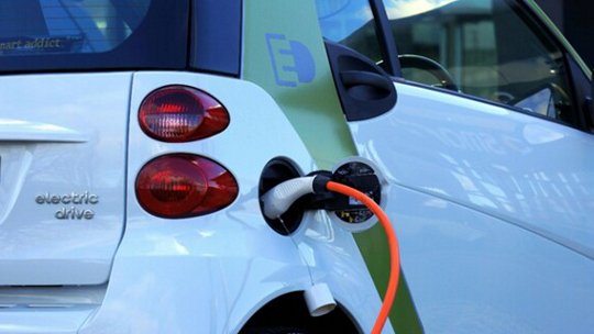 Un véhicule électrique compact blanc est montré en train de charger, avec un câble orange vif connecté à son port de charge.
