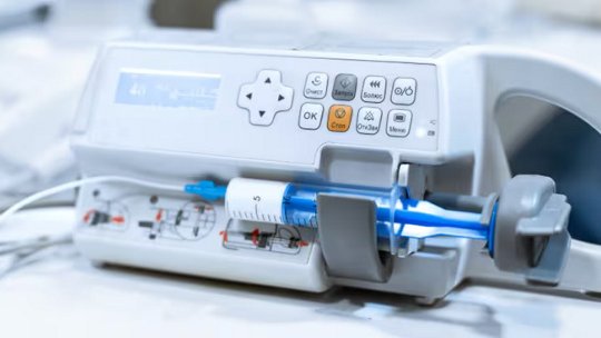 Una moderna pompa per infusione medica è mostrata in primo piano, con una siringa trasparente inserita nel dispositivo.