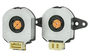 Two compact rotary encoders are shown side by side, each featuring a circular metallic housing and a central orange component. The encoders have visible electrical connectors at the bottom, designed for integration into electronic systems. The background is plain, highlighting the technical details and mechanical structure of the devices.