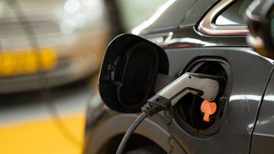 A close-up view of an electric vehicle being charged, with the charging cable plugged into the car's port.