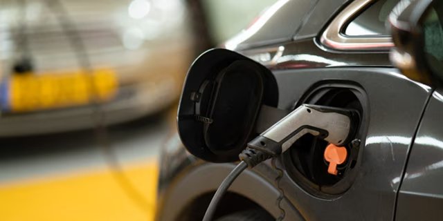 A close-up view of an electric vehicle being charged, with the charging cable plugged into the car's port.