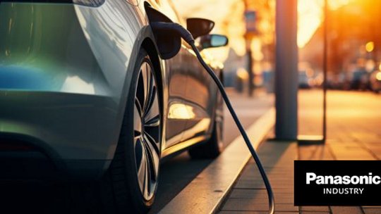 一辆现代电动车在日落时分停在城市街道上的充电站充电。右下角清晰可见Panasonic Industry标志。