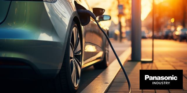 一辆现代电动车在日落时分停靠在城市街道上的充电站充电。右下角清晰可见Panasonic Industry标志。