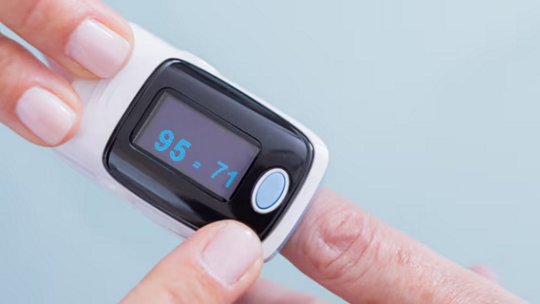 Una persona utilizza un pulsossimetro su un dito, mostrando una lettura di 95=71.