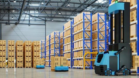 A small quadcopter drone hovers in the foreground of a spacious warehouse. 