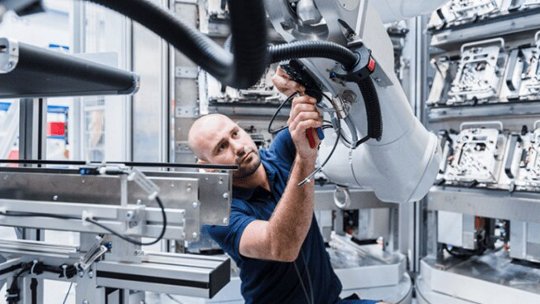 A technician is working closely with a large robotic arm in a modern industrial facility.