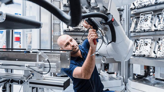 A technician is working closely with a large robotic arm in a modern industrial facility.