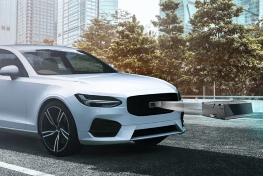 A modern white sedan is parked on an urban street with a large sensor or scanning device extending from its front grille.