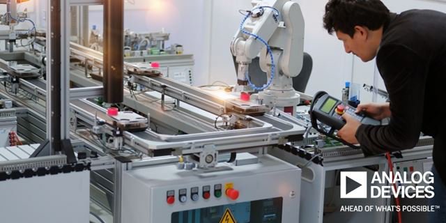 An engineer is seen working with a robotic arm in a modern industrial environment. The workspace features advanced machinery, control panels, and automated systems. The engineer is using a handheld device to interact with the equipment.
