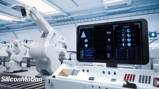 Un environnement industriel moderne présente plusieurs bras robotiques opérant dans un environnement propre et de haute technologie. Au premier plan, un panneau de contrôle avec un grand affichage numérique présente diverses données et analyses de système. Le logo SiliconMotion est clairement visible dans le coin inférieur gauche.