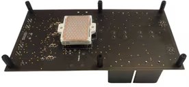 Bottom view of EVBUM2878G: A rectangular electronic circuit board is shown with a single large component mounted near the center. The board features multiple visible solder points and four black standoffs at the corners.