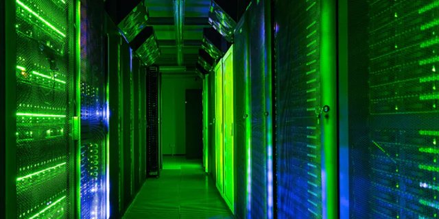 A brightly lit corridor in a data center features rows of server racks glowing with green and blue LED lights.