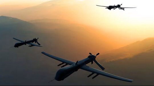 Three large drones flying in formation over a mountainous landscape during sunset.