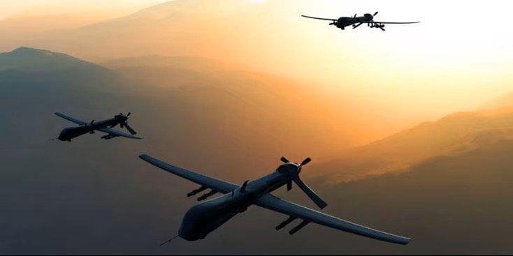 Three military drones flying in formation over a mountainous landscape at sunset, illustrating counter-drone defense technology.