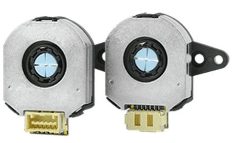 Image shows two small, identical rotary encoder sensors side by side. Each unit has a circular central aperture with a blue crosshair-like pattern. The encoders feature metallic housings with plastic mounting tabs and visible connector ports at the bottom. The background is plain and neutral, emphasizing the electronic components.