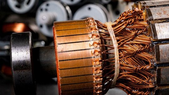 A detailed view of an electric motor rotor showcases tightly wound copper wires and metallic components. The image highlights the intricate construction of the rotor, with other motor parts visible in the blurred background.