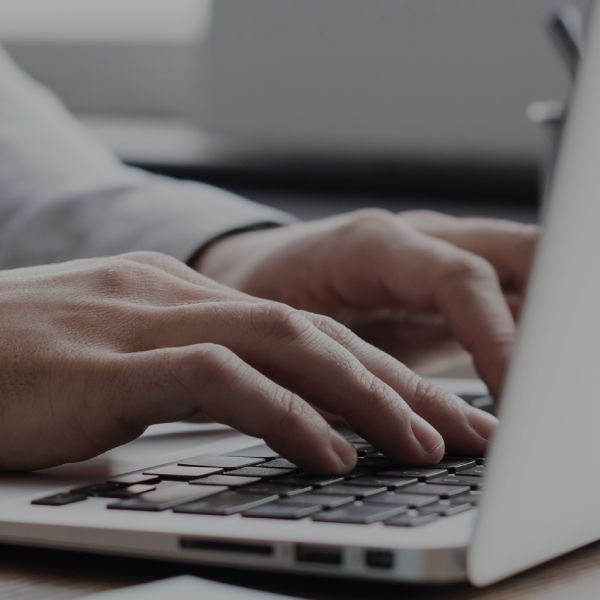 在专业环境中，双手在银色笔记本电脑上打字的特写镜头。