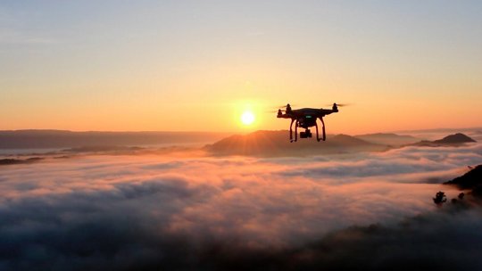 Image of drone flying above clouds at sunrise