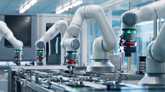 Multiple white industrial robotic arms operate along an automated production line in a modern factory environment.