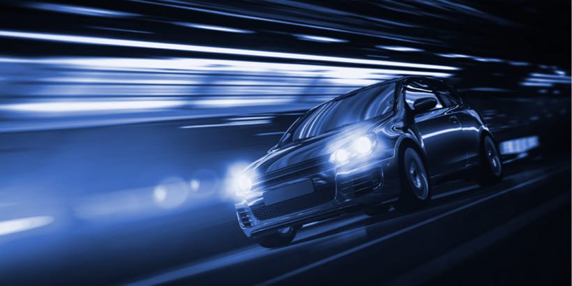 A modern compact car is captured in motion, racing through a tunnel with dynamic blue lighting. 