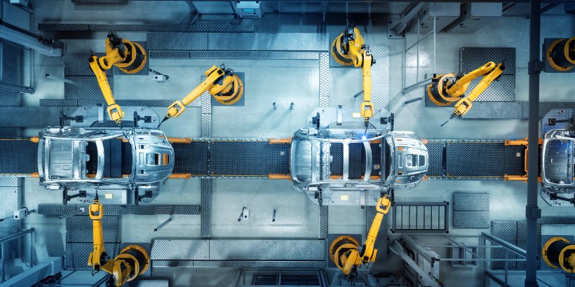Overhead view of an automotive production line shows multiple robotic arms working on car bodies. 