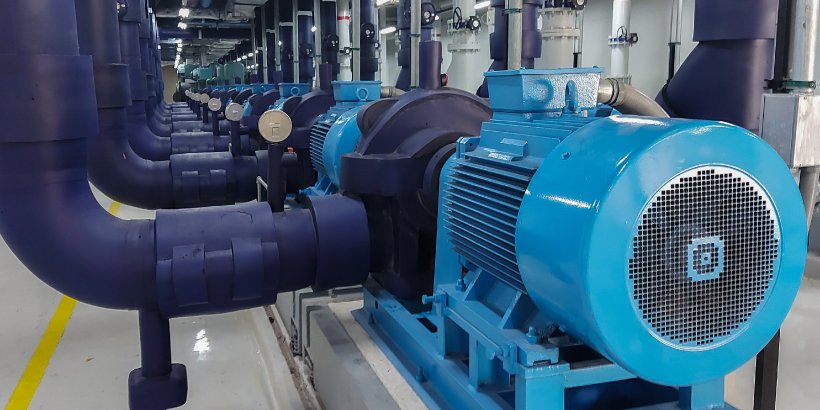 A row of large blue electric motors is installed along a brightly lit industrial corridor. 