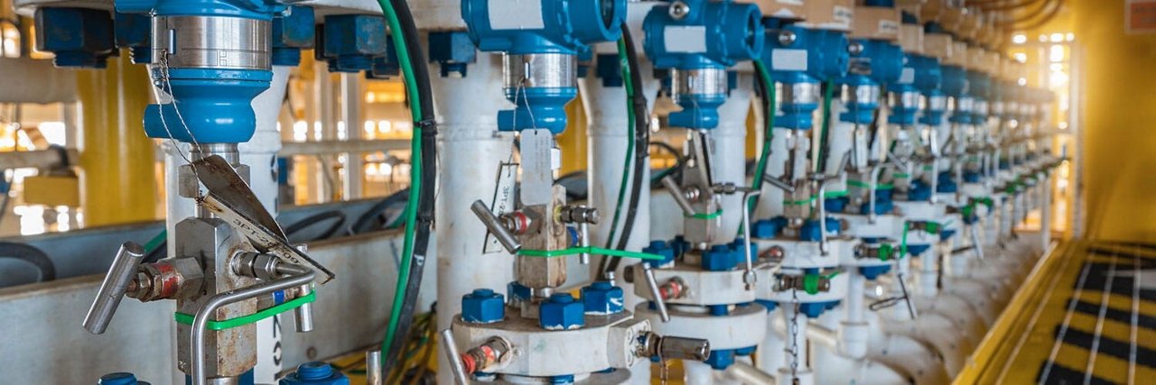 工厂环境中，一排工业管道配备了蓝色阀门控制器和仪表。