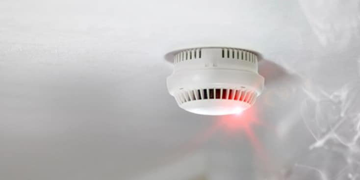 Image of a smoke detector with red light and smoke in the air