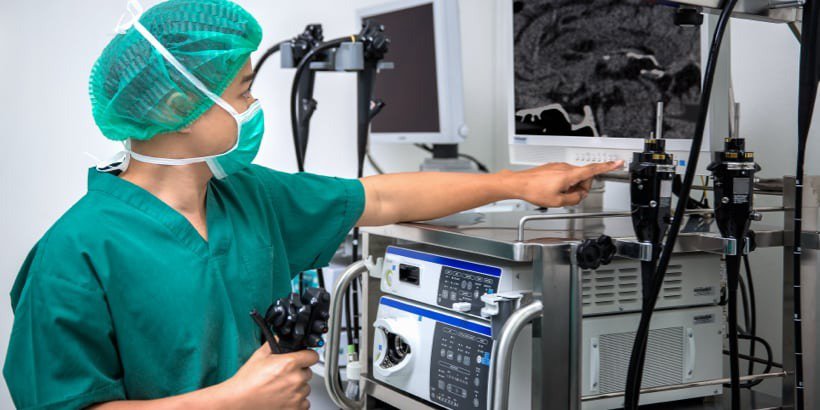 A healthcare professional in green scrubs operates advanced endoscopy equipment in a clinical setting.