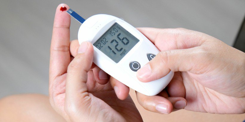 A close-up of a hand using a digital blood glucose meter to measure sugar levels.
