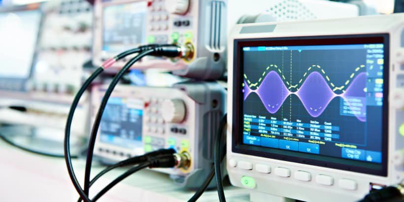Close-up of multiple digital oscilloscopes displaying waveforms on their screens in a laboratory environment.
