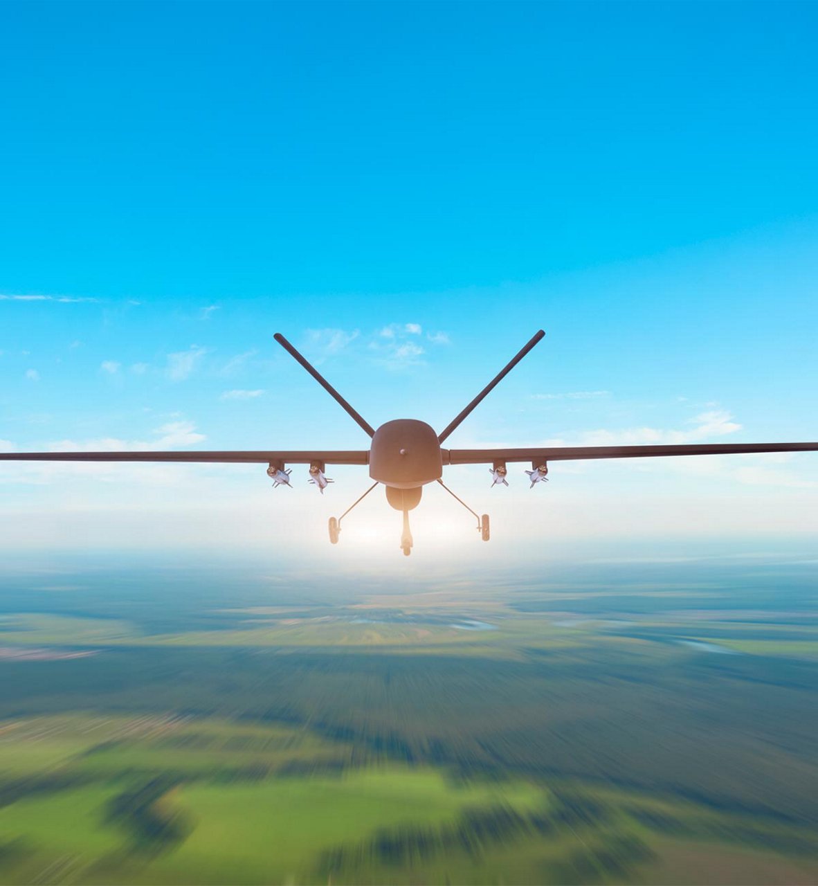 Un gran dron aéreo no tripulado es captado desde atrás mientras vuela a gran altura sobre un vasto paisaje rural.