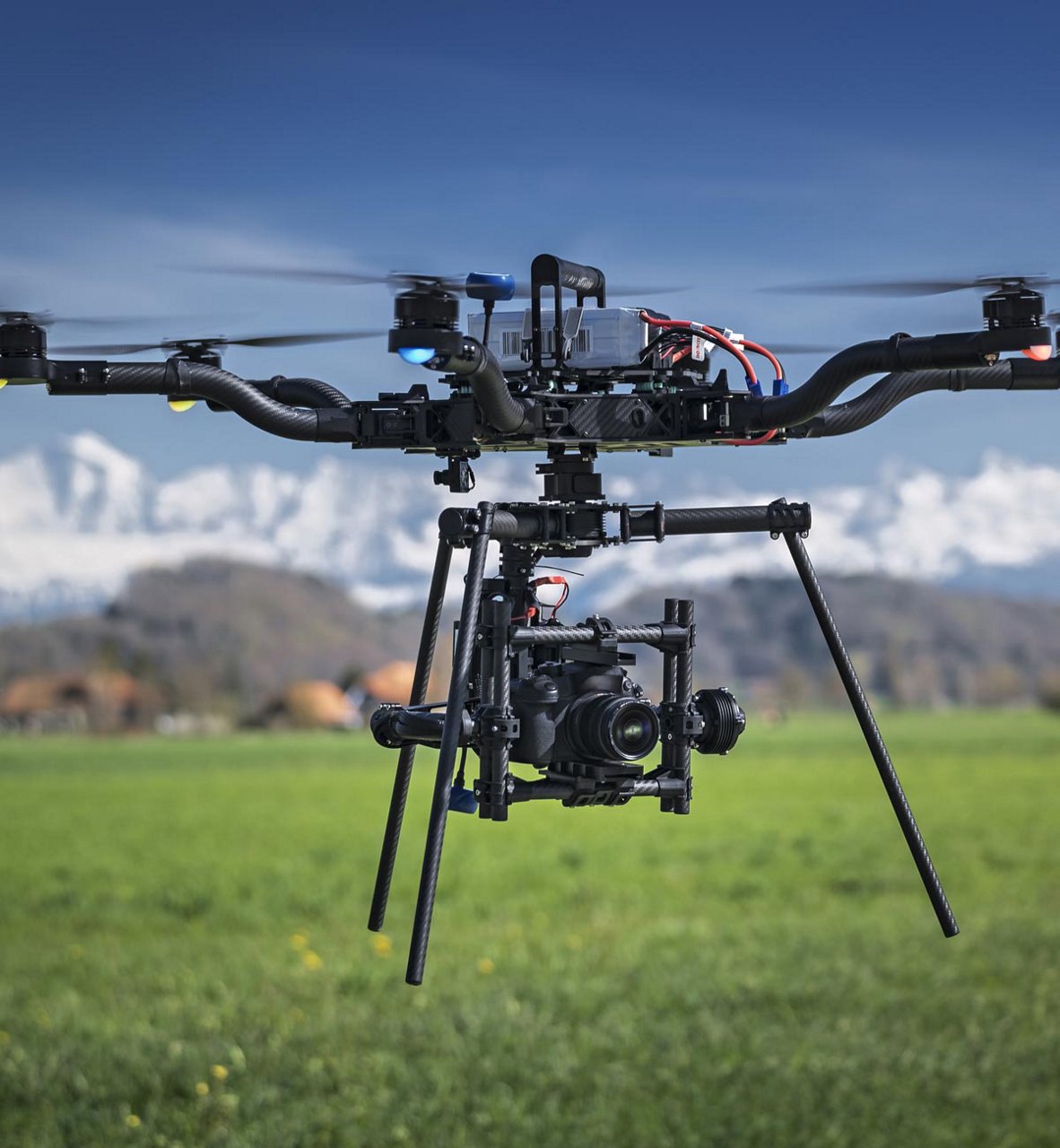 Un gran dron multirrotor equipado con un equipo de cámara profesional se cierne sobre un campo verde y herboso.