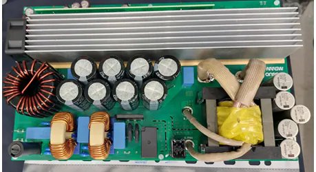 This image shows the internal layout of an electronic circuit board, featuring multiple capacitors, coils, and a large heat sink. The setting appears to be a technical or repair environment, with a clear view of the board's components and wiring.