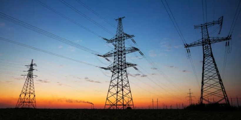 A series of high-voltage power lines stretch across a rural landscape during sunset. 