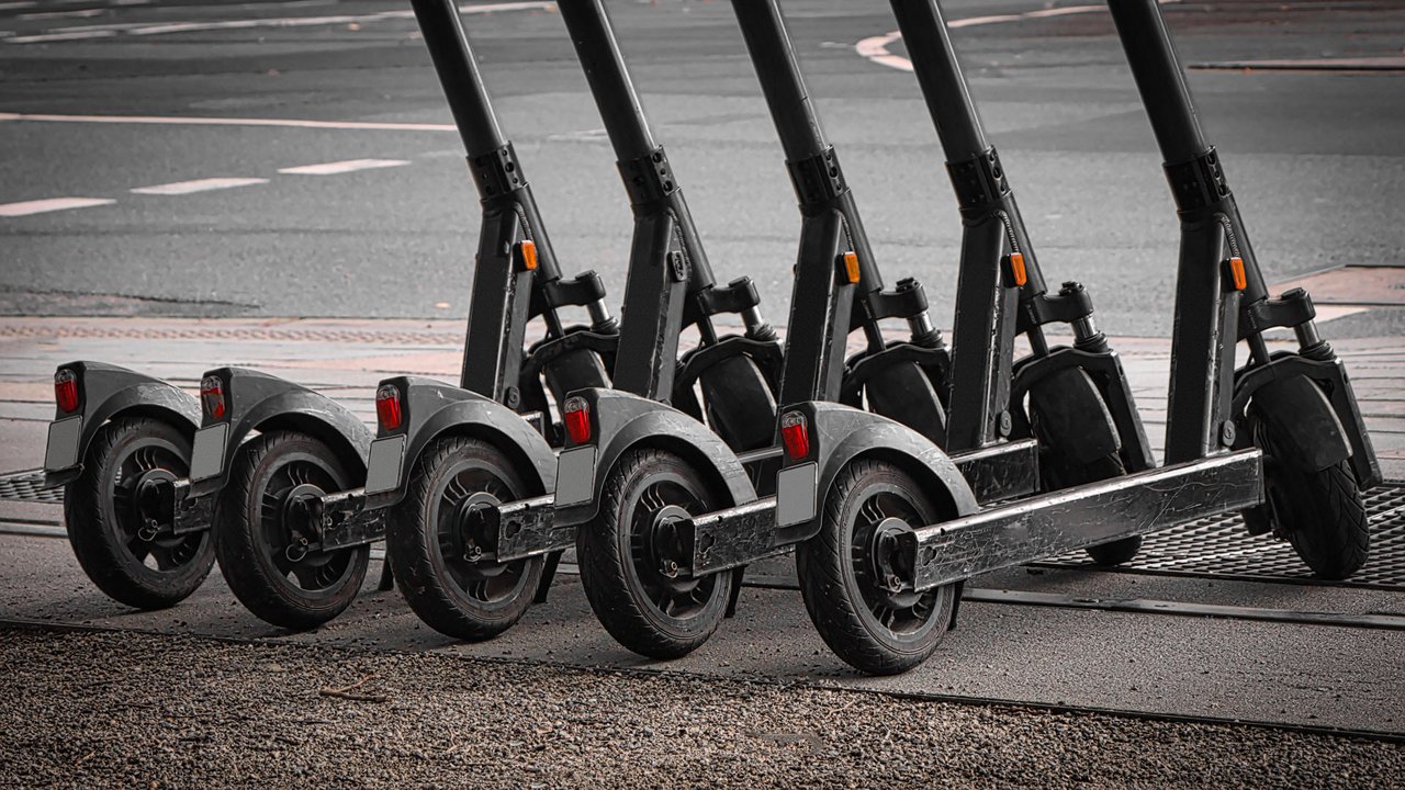 A lineup of modern electric scooters arranged neatly on a paved surface near a crosswalk. 