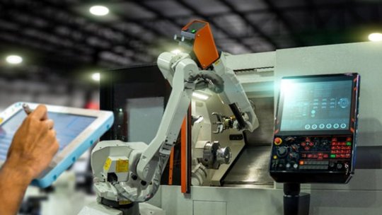 Un braccio robotico opera in un ambiente di produzione ad alta tecnologia, interagendo con un pannello di controllo e macchinari