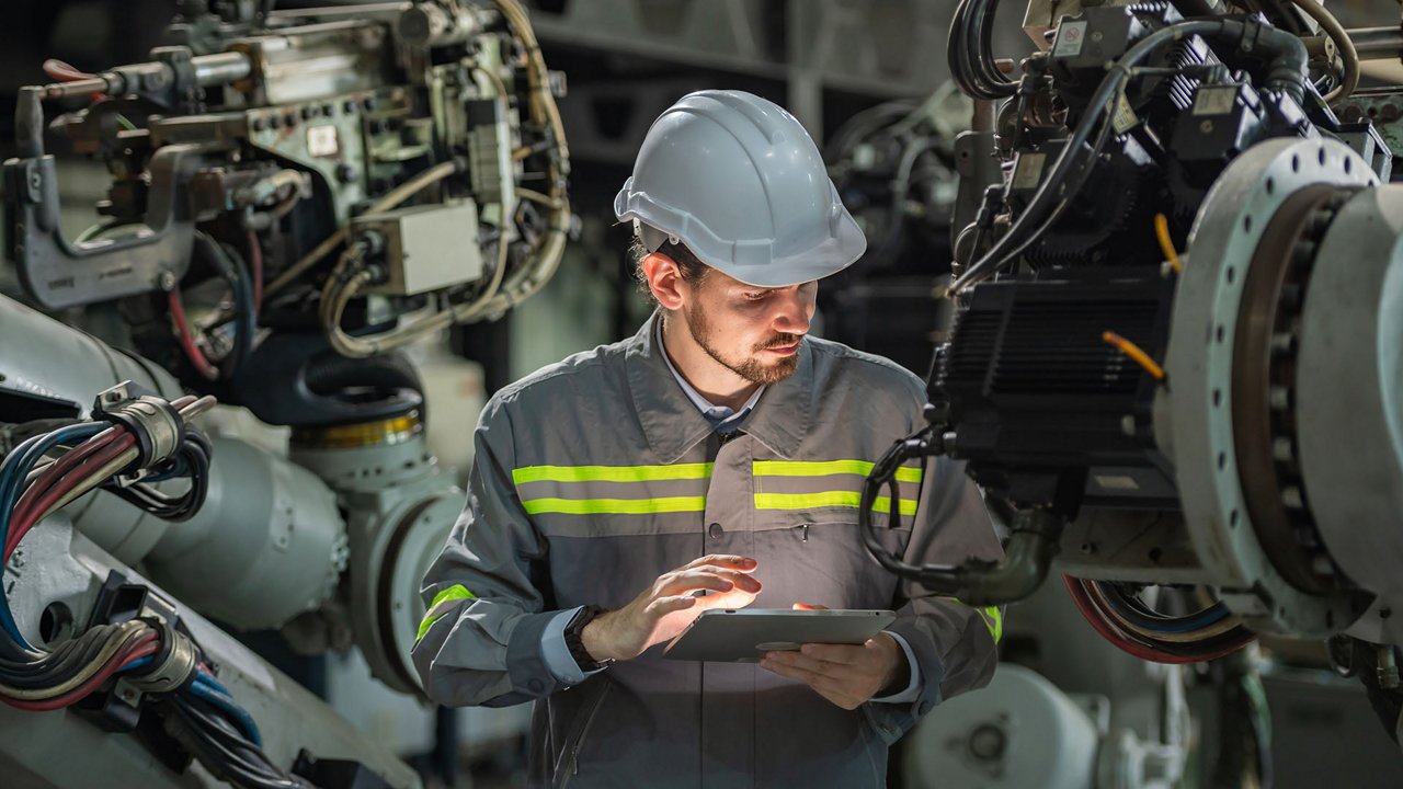 Male automation engineer in uniform helmet safety inspection check control heavy machine robot arm system in industrial factory. technician worker check for repair factory machine